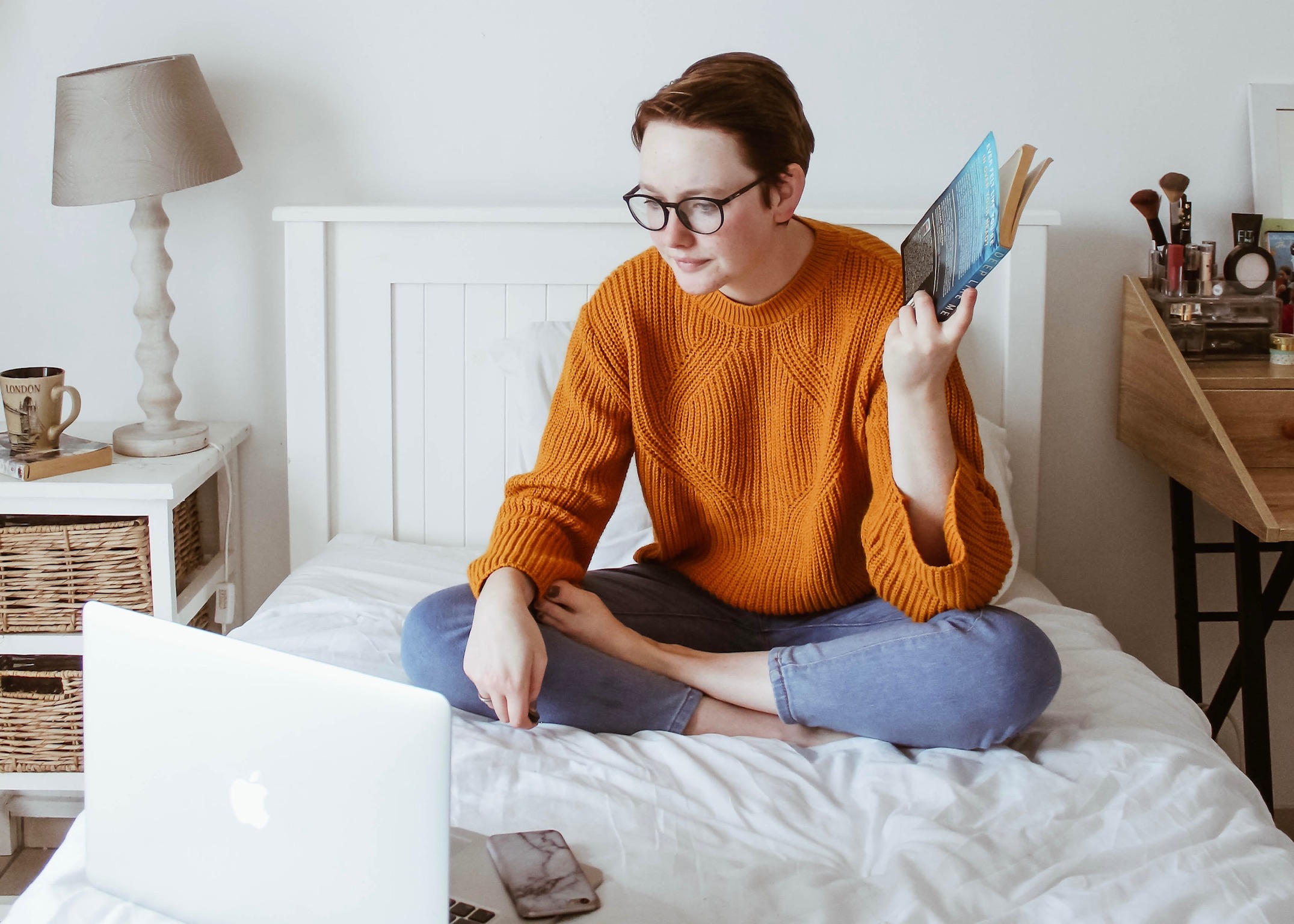 A young lady sitting crossed legged on a single bed looking at a laptop computer 